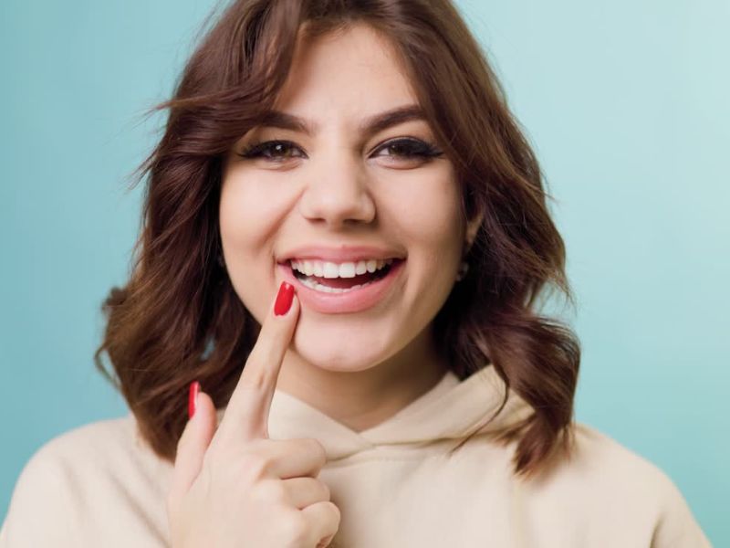 devojka sa belim zubima se veselo smeši i pokazuje prstom u zube
